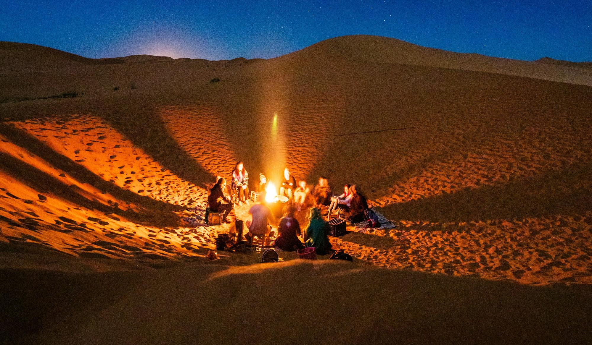 Friends gathered around a fire among desert dunes at night